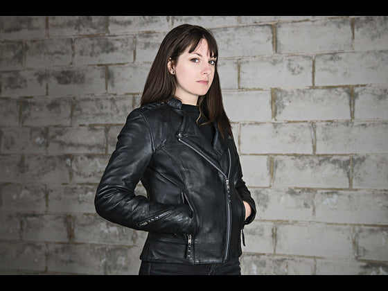 "Smiling woman in a sleek leather motorcycle jacket, hands casually tucked in pockets, exuding confident style and attitude."